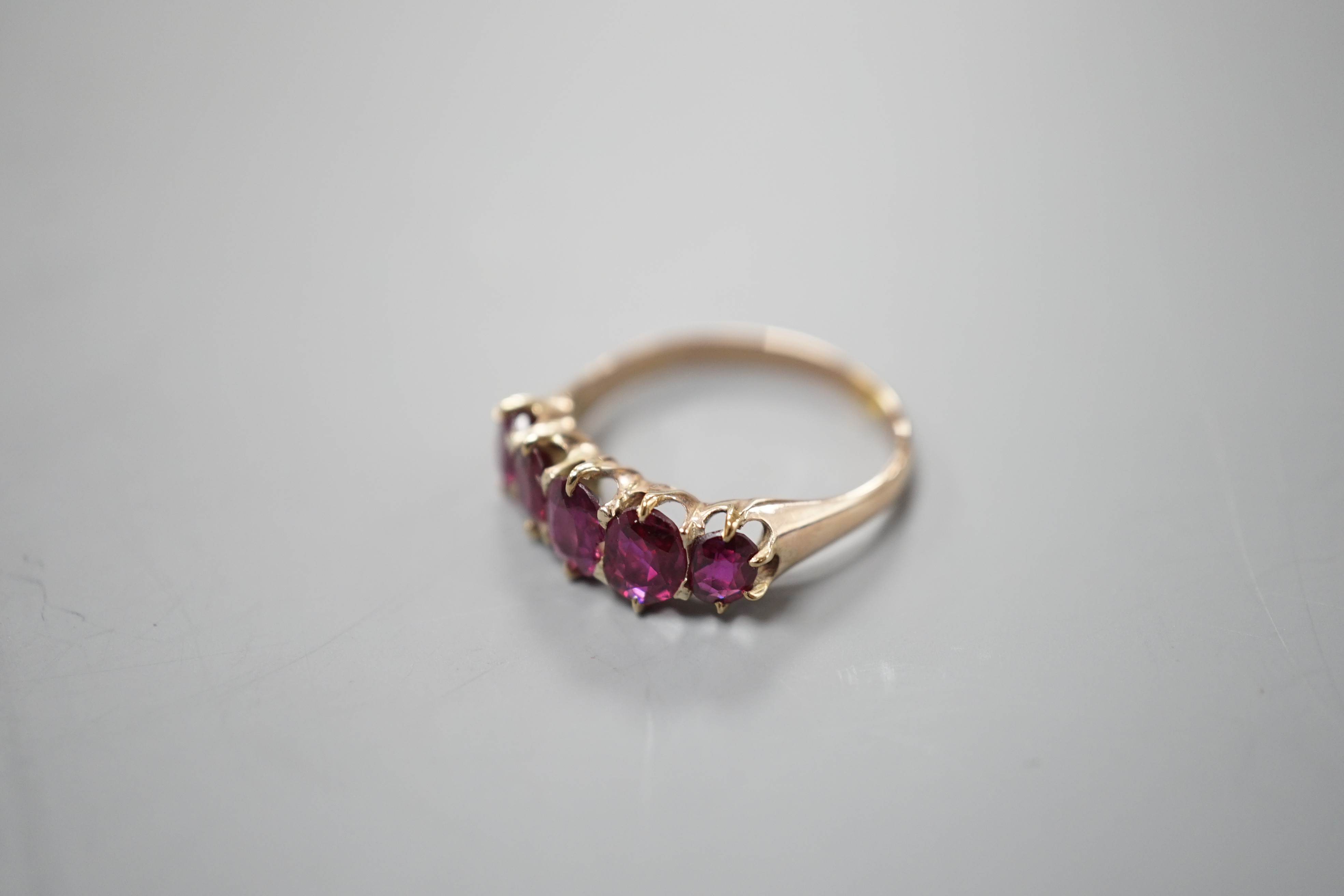 An early 20th century yellow metal and graduated five stone ruby set half hoop ring, size O, gross weight 2.6 grams.